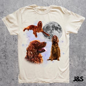 K&ouml;nnte beinhalten: Cremefarbenes T-Shirt mit einem grafischen Design von drei Irish Setter Hunden, einem Vollmond und einem Sternenhintergrund. Die Hunde sind in verschiedenen Posen dargestellt, einer davon in der Luft. Das Shirt hat einen Rundhalsausschnitt und kurze &Auml;rmel.