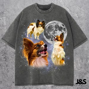 May include: Dark gray t-shirt featuring a graphic of three Papillon dogs with a full moon and starry background. The dogs are in shades of brown, white, and tan. The text "J&S Essential" is at the bottom right.