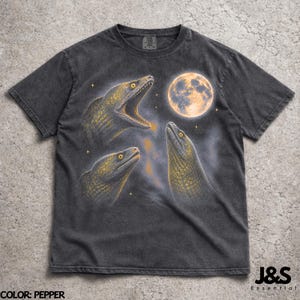 May include: Pepper-colored t-shirt featuring a graphic of three moray eels with yellow eyes and open mouths, set against a night sky with a full moon. The shirt has a vintage, washed look.