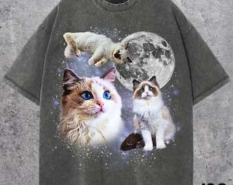 Pode incluir: T-shirt cinza escuro com um gráfico de três gatos Ragdoll com olhos azuis, uma lua cheia e um fundo estrelado. A camisa tem gola redonda e mangas curtas. O texto "J&S Essential" está no canto inferior direito.