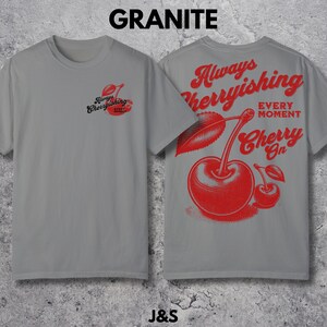 May include: A gray t-shirt with a red cherry graphic on the front and back. The front graphic says "Always Cherryishing Every Moment". The back graphic says "Always Cherryishing Every Moment Cherry On".