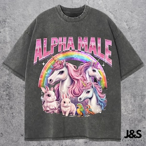 以下が含まれることがあります： 「ALPHA MALE」の文字と虹、ユニコーン、ウサギ、オウムのイラストが描かれた、濃いグレーのTシャツ。 ヴィンテージ感のあるウォッシュ加工が施されています。