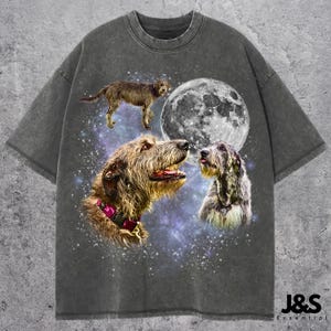 May include: Dark gray t-shirt featuring a graphic of three dogs with a full moon and a starry background. The dogs are in shades of brown and gray, with one wearing a pink collar. The shirt has a vintage, distressed look.