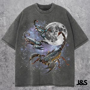 Könnte beinhalten: Dunkelgraues T-Shirt mit einem Himmelsdesign. Es zeigt drei detaillierte Skorpione in Schwarz, Blau und Gelb, vor einem Vollmond und Sternenhimmel. Das T-Shirt hat eine lockere Passform und einen Rundhalsausschnitt.