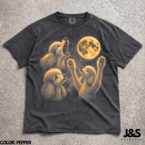 May include: Pepper-colored t-shirt featuring a graphic of three poodles with a full moon in the background. One poodle is howling, another is looking up, and the third has its paws raised. The text "J&S Essential" is in the lower right corner.