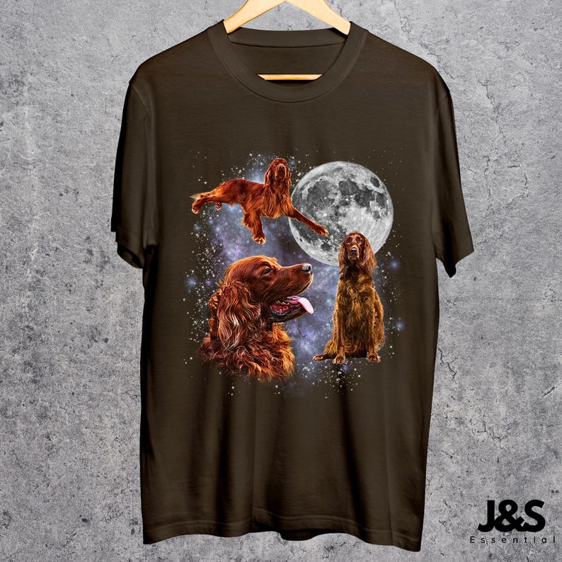 K&ouml;nnte beinhalten: Dunkelbraunes T-Shirt mit Illustrationen von Irish Setter Hunden, einem Vollmond und einem Sternenhimmel. Das Design zeigt drei Hunde in verschiedenen Posen. Das T-Shirt h&auml;ngt an einem Holzkleiderb&uuml;gel.