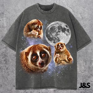 May include: Dark gray t-shirt featuring a design with three slow lorises, a full moon, and a starry background. The slow lorises are brown and white, with large eyes. The text "J&S Essential" is at the bottom right.