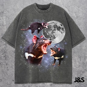 May include: Dark gray t-shirt featuring a graphic of three Tasmanian devils with open mouths against a starry background and a full moon. The shirt has a distressed, vintage look, with the text "J&S Essential" at the bottom.