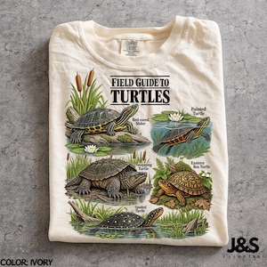 Peut inclure: Un t-shirt ivoire avec un motif intitulé Field Guide to Turtles. Le design présente des illustrations d'une tortue à tempes rouges, d'une tortue peinte, d'une tortue serpentine, d'une tortue boîte et d'une tortue ponctuée avec leurs noms.