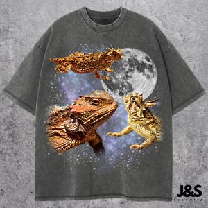 May include: Dark gray t-shirt featuring a graphic of three horned lizards with a full moon and starry background. The lizards are in shades of brown, orange, and yellow. The text "J&S Essential" is at the bottom.