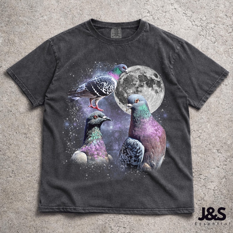 Puede incluir: Camiseta gris oscuro con un dise&ntilde;o de tres palomas coloridas sobre un cielo estrellado y una luna llena. Las aves tienen plumas iridiscentes en tonos morados, verdes y grises. La camiseta tiene un aspecto vintage.