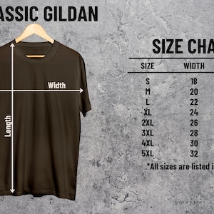 Puede incluir: Una camiseta marr&oacute;n colgada de una percha de madera, con una tabla de tallas. La tabla muestra las tallas S a 5XL, con medidas de ancho y largo en pulgadas. El texto "CLASSIC GILDAN" est&aacute; en la parte superior.