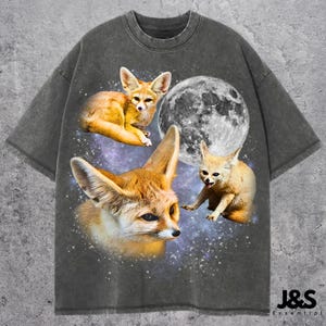 Op de afbeelding: Donkergrijs T-shirt met een afbeelding van drie fennek vossen, een volle maan en een sterrenhemel. Het shirt heeft een vintage was effect en de tekst "J&S Essential" staat rechtsonder.