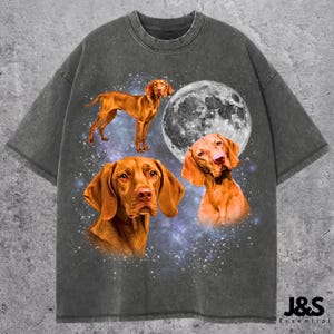 May include: Dark gray t-shirt featuring a design of three Vizsla dogs, a full moon, and a starry background. The shirt has a distressed, vintage look. The brand name "J&S Essential" is printed at the bottom right.