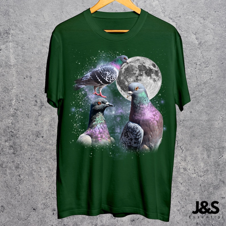 Puede incluir: Camiseta verde oscuro con un dise&ntilde;o de tres palomas con plumas iridiscentes, una luna llena y un fondo estrellado. La camiseta tiene cuello redondo y mangas cortas. La marca "J&S Essential" est&aacute; impresa en blanco en la parte inferior derecha.