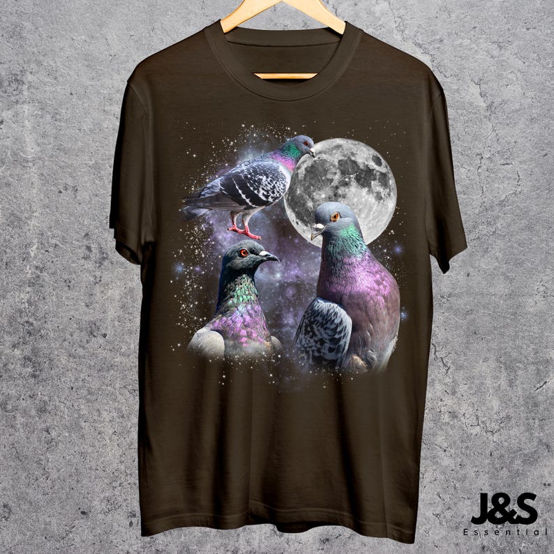 Puede incluir: Camiseta marr&oacute;n con un dise&ntilde;o de tres palomas coloridas frente a una luna llena. Las aves tienen plumas iridiscentes en tonos morados, verdes y azules. La camiseta est&aacute; colgada en una percha de madera.