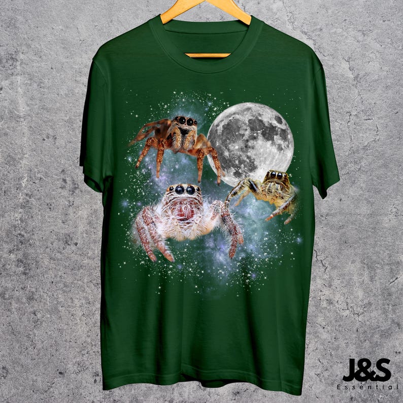 May include: Green t-shirt featuring a design of three jumping spiders with a full moon in the background. The spiders are brown and white, with detailed textures. The shirt has the text "J&S Essential" at the bottom.