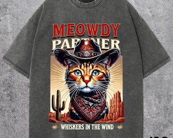 Peut inclure: Un t-shirt gris avec un motif vintage d'un chat portant un chapeau de cowboy et un bandana. Le texte sur le t-shirt est "MEOWDY PARTNER" et "WHISKERS IN THE WIND".