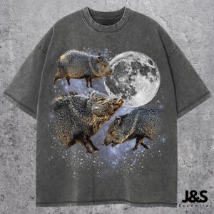 May include: Dark grey t-shirt with a graphic of three peccaries, a full moon, and a starry sky. The shirt has a vintage wash effect and a crew neck. The brand logo "J&S Essential" is at the bottom right.