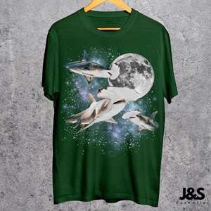 Puede incluir: Camiseta verde con un dise&ntilde;o de tiburones nadando en el espacio, con una luna llena en el fondo. La camiseta tiene cuello redondo y mangas cortas. El dise&ntilde;o incluye tiburones martillo y otras especies de tiburones.