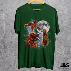 K&ouml;nnte beinhalten: Dunkelgr&uuml;nes T-Shirt mit drei Illustrationen von Irish Setter Hunden und einem Vollmond. Die Hunde sind in verschiedenen Posen dargestellt, darunter einer in der Luft, einer mit herausgestreckter Zunge und einer sitzend. Der Text "J&S Essential" ist sichtbar.