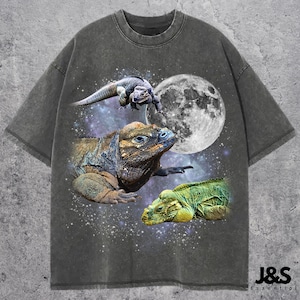 Op de afbeelding: Donkergrijs T-shirt met een afbeelding van drie hagedissen, een volle maan en een sterrenhemel. De hagedissen zijn in tinten groen, bruin en grijs. De tekst "J&S Essential" staat rechtsonder.