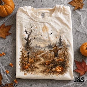 Könnte beinhalten: Ein elfenbeinfarbenes T-Shirt mit einem detaillierten Grafikdruck einer herbstlichen Ernteszene. Das Motiv zeigt eine Vogelscheuche in einem Kürbisfeld mit einem gewundenen Pfad, einem großen kahlen Baum, einem Vollmond und einer fliegenden Fledermaus.