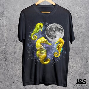 Może przedstawiać: Czarny t-shirt z trzema ż&oacute;łtymi konikami morskimi, pełnią księżyca i gwiezdnym tłem. Koniki morskie mają ż&oacute;łte i zielone kolory. Koszulka wisi na drewnianym wieszaku.