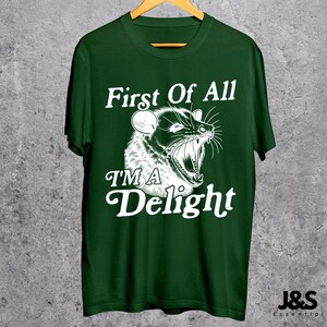 May include: A dark green t-shirt with a white graphic of an animal with the text "First Of All I'm A Delight".