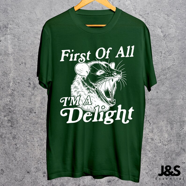May include: A dark green t-shirt with a white graphic of an animal with the text "First Of All I'm A Delight".