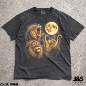 May include: Pepper-colored t-shirt featuring a graphic of three lions and a full moon. The lions are depicted in shades of brown and gold, with one roaring, one looking up, and one with its paws raised. The text "J&S Essential" is visible.