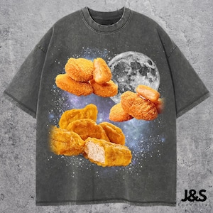 May include: Dark gray t-shirt featuring a graphic of fried chicken nuggets, a full moon, and a starry sky. The shirt has a crew neck and short sleeves. The text "J&S Essential" is printed on the bottom right.
