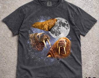 Peut inclure: T-shirt gris foncé avec un motif de trois morses, une pleine lune et un fond étoilé. Les morses sont représentés en nuances de marron et de beige, avec des défenses proéminentes. Le t-shirt a un aspect vintage et vieilli.