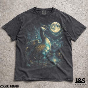 Pode incluir: Camiseta cor pimenta com um ganso e uma cena noturna iluminada pela lua. O design inclui uma lua cheia, estrelas e água. A camiseta tem uma lavagem vintage. O texto "J&S Essential" é visível.