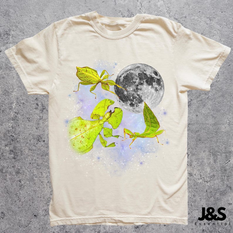 May include: Cream-colored t-shirt featuring a whimsical design. The graphic includes a full moon, leaf insects, and a starry background. The shirt has a classic crew neck and short sleeves. The brand logo is in the bottom right corner.