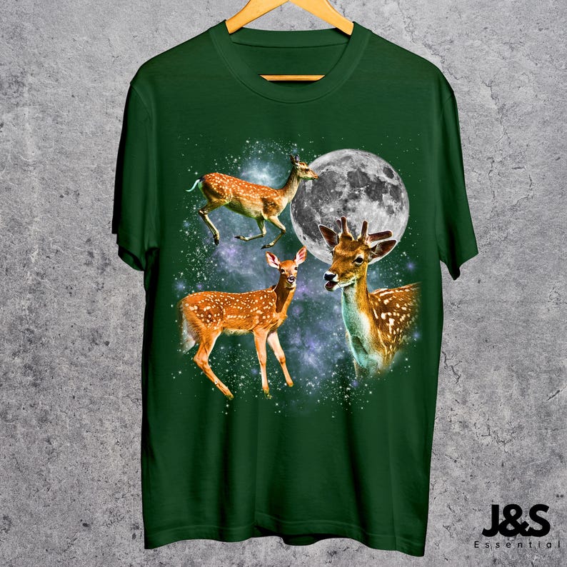 May include: Green t-shirt featuring a design of three deer with a full moon and a starry background. The deer are brown with white spots. The text "J&S Essential" is at the bottom right.