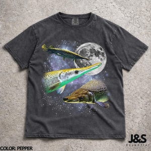 May include: Pepper-coloured t-shirt featuring a graphic design of three garfish set against a starry night sky and a full moon. The design includes the text "J&S Essential".