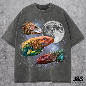 May include: Dark grey t-shirt with a graphic of three lizards, a full moon, and a starry background. The lizards are in shades of red, orange, yellow, green, and blue. The text "J&S Essential" is at the bottom.