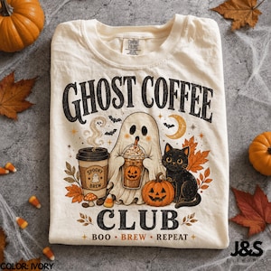 Peut inclure: Un t-shirt ivoire avec un motif portant le texte GHOST COFFEE CLUB et BOO BREW REPEAT. Le design comprend un fantôme tenant une tasse de café, un chat noir, des citrouilles, des feuilles d'automne et des chauves-souris. Étiquette Comfort Colors.