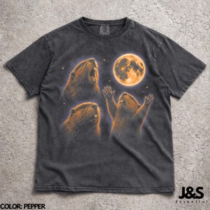 Könnte beinhalten: Dunkelgraues T-Shirt mit einem Aufdruck von drei Bibern und einem orangefarbenen Mond. Die Biber sind in verschiedenen Posen dargestellt. Das T-Shirt hat einen Vintage-Look. Der Text "J&S Essential" ist unten rechts zu sehen.