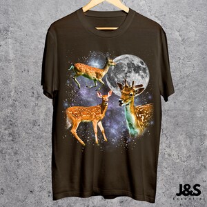 May include: Brown t-shirt featuring a graphic of three deer against a backdrop of a full moon and a starry galaxy. The deer have brown fur with white spots. The text "J&S Essential" is at the bottom right.
