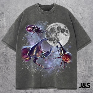 May include: Charcoal grey t-shirt with a graphic of three beetles, a full moon, and a starry sky. The shirt has a worn appearance, and the text "J&S Essential" is printed at the bottom right.
