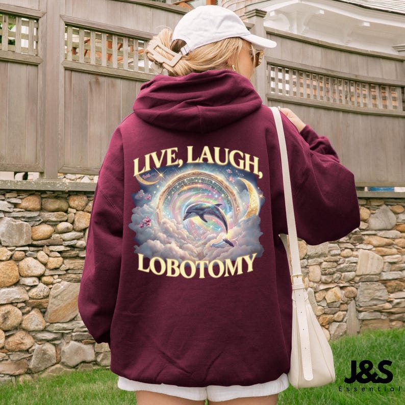 May include: Burgundy hoodie with the words "LIVE, LAUGH, LOBOTOMY" in white. The graphic features a dolphin leaping through a rainbow-colored portal, surrounded by clouds and moons. The hoodie is a pullover style.