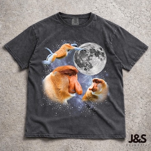 May include: Dark gray t-shirt featuring a graphic of proboscis monkeys with a full moon and starry background. The design includes three monkeys, one reaching for the moon. The shirt has a vintage, worn look.