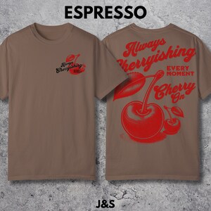 May include: A brown t-shirt with a red cherry graphic on the back. The graphic says "Always Cherryishing Every Moment Cherry On". The front of the shirt has a smaller version of the cherry graphic with the text "Always Cherryishing Every Moment".