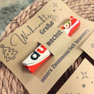 K&ouml;nnte beinhalten: Eine Karte aus Kraftpapier mit den Worten "Weihnachts Gr&uuml;&szlig;e" und einer Weihnachtsbaum-Illustration. Ein rot-wei&szlig;er Schokoriegel ist teilweise in einen Schlitz in der Karte gesteckt. Die Karte hat auch die Worte "du machst unsere Zusammenarbeit besonders."