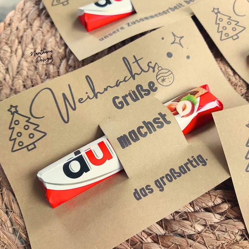 K&ouml;nnte beinhalten: Kraftpapierkarten mit Weihnachtsgr&uuml;&szlig;en und einem Kinder Bueno Schokoriegel. Die Karten haben ein Weihnachtsbaumdesign und die Worte "Weihnachts Gr&uuml;&szlig;e" und "machst das gro&szlig;artig" in Schwarz gedruckt.