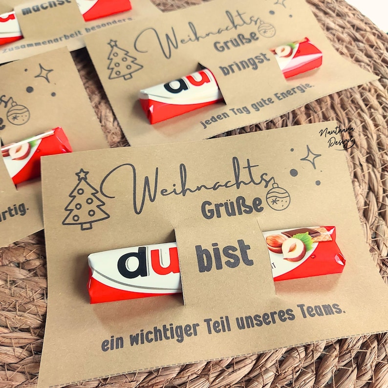 K&ouml;nnte beinhalten: Karten aus Kraftpapier mit Weihnachtsgr&uuml;&szlig;en und Schokoriegeln. Die Karten zeigen eine Weihnachtsbaum-Illustration und die Worte "Weihnachts Gr&uuml;&szlig;e" und "du bist". Die Schokoriegel sind rot, wei&szlig; und schwarz.