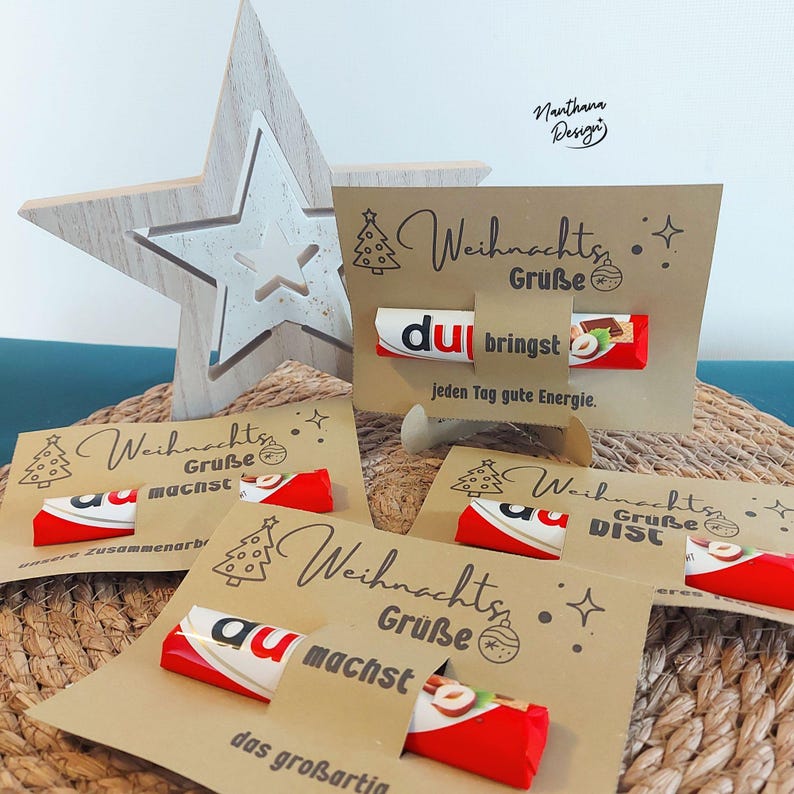 K&ouml;nnte beinhalten: Weihnachtsgru&szlig;karten aus Kraftpapier mit einem Kinder Bueno Schokoriegel. Die Karten haben ein Weihnachtsbaum- und Sterndesign mit deutschem Text. Im Hintergrund befindet sich ein Holzstern.