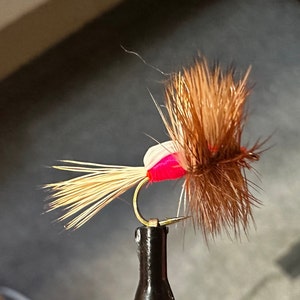 May include: A pink and white fly fishing lure with brown feathers and a gold hook.